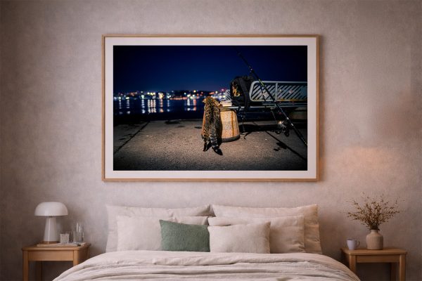 Fotografie über einem Bett: nächtlicher Pier mit Katze, Angelruten, Bank und Stadtlichtern am Wasser