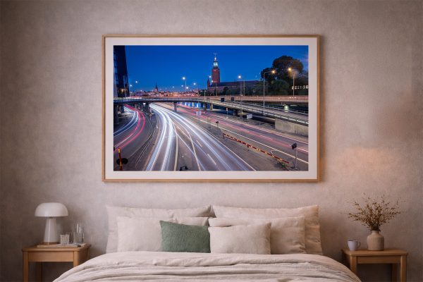 Panoramafoto mit Lichtspuren des Nachtverkehrs auf mehrspuriger Straße, beleuchtete Stadt im Hintergrund, gerahmt über einem Bett im Schlafzimmer
