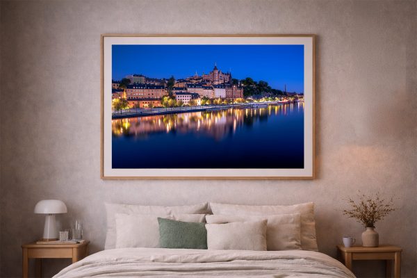 Großes gerahmtes Foto einer beleuchteten Uferstadt bei Nacht über einem Bett in einem dezent eingerichteten Schlafzimmer.