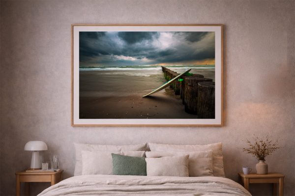 Fotografie mit Surfbrett an einer Reihe Holzpfähle im Meer, aufgehängt über einem Bett in einem sanft beleuchteten Schlafzimmer