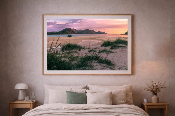 Großer gerahmter Fotodruck eines ruhigen Strandes mit Grasinseln und Bergen im Sonnenuntergang über einem gemütlichen Bett im Schlafzimmer