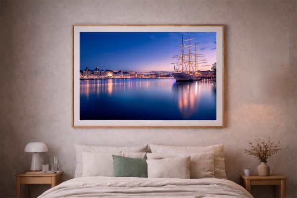 Fotografie eines beleuchteten Segelschiffs im Hafen bei blau-violetter Dämmerung, als gerahmtes Wandbild über einem Bett im Schlafzimmer