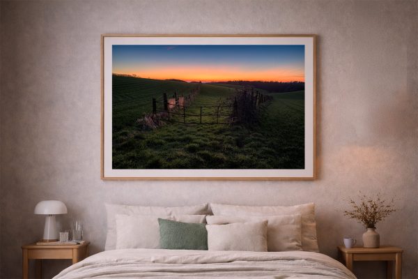 Großes Landschaftsfoto mit Wiese und altem Zaun im Abendlicht über einem Bett in einem ruhigen Schlafzimmer