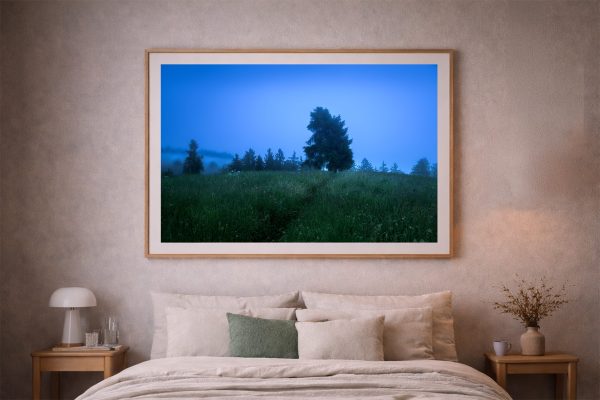Großer gerahmter Kunstdruck mit blauer nebliger Wiesenlandschaft über einem beige eingerichteten Bett im Schlafzimmer.