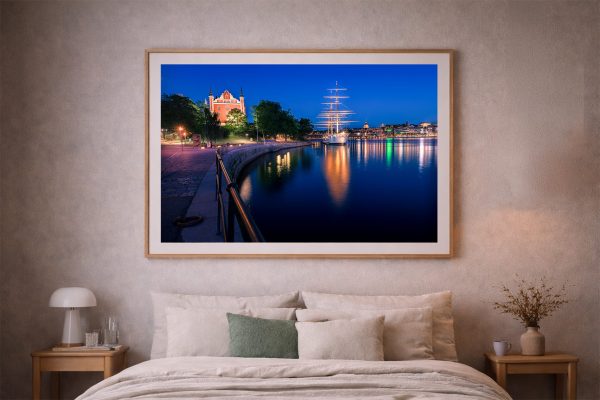 Großer gerahmter Fotokunstdruck über einem Bett zeigt einen nächtlichen Hafen mit beleuchtetem Segelschiff und Uferpromenade.