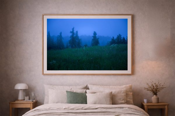 Großer gerahmter Fotodruck einer nebligen Waldwiese in tiefem Blau über einem beige eingerichteten Bett im Schlafzimmer.