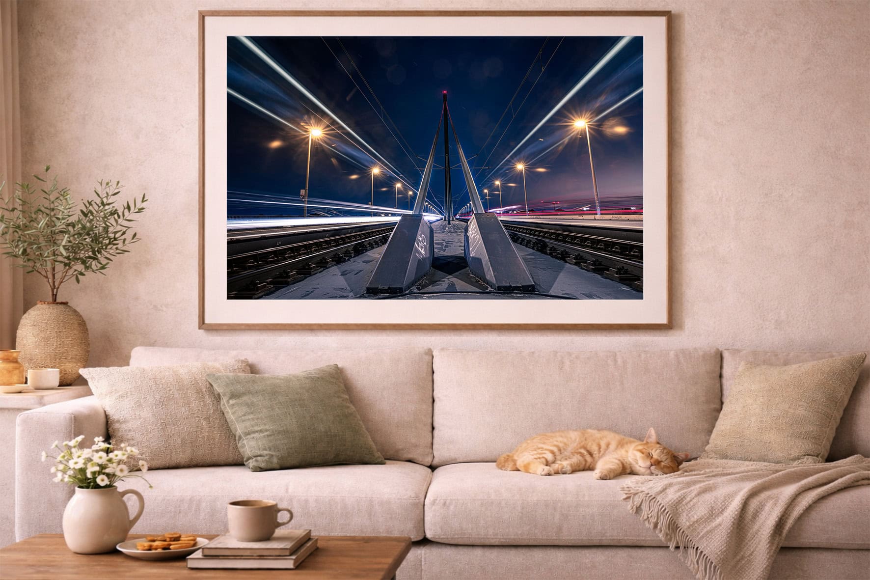 Großes Wandbild mit nächtlicher Bahntrasse und Lichtspuren über einem beigen Sofa mit Kissen und schlafender Katze im Wohnzimmer