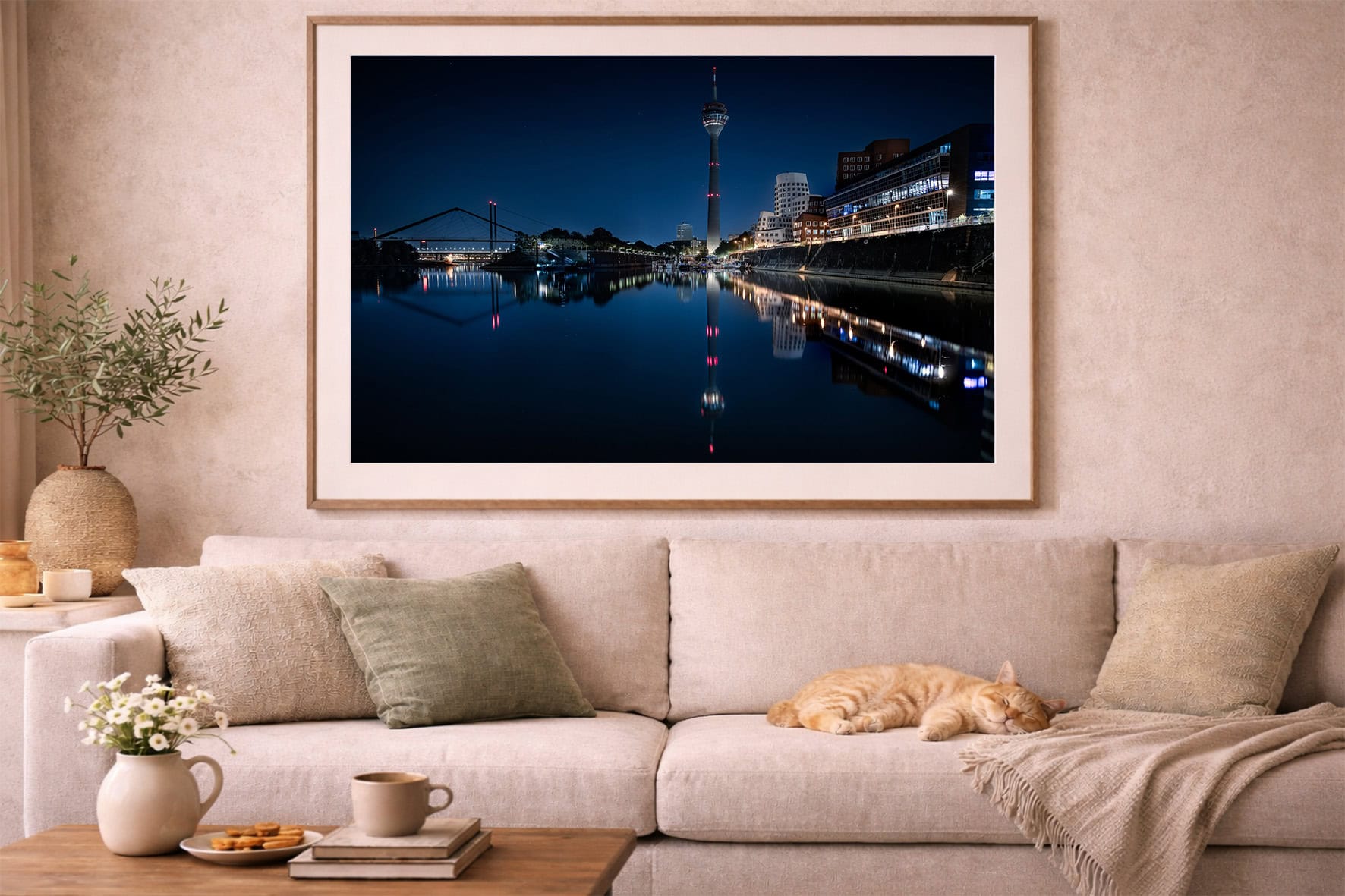 Großer gerahmter Fotodruck einer nächtlichen Stadt am ruhigen Fluss über beiger Sofa-Landschaft mit Katze