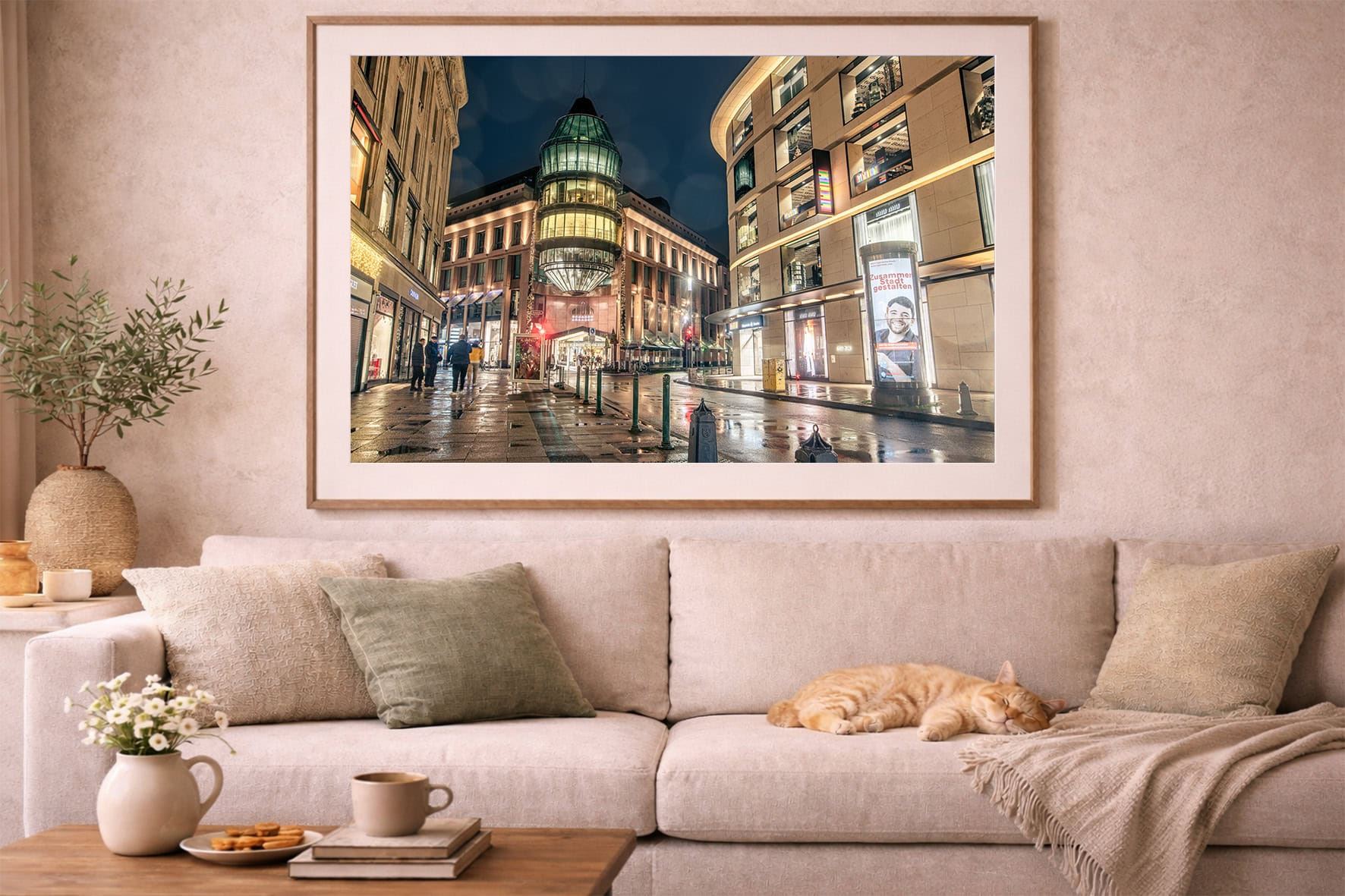 Fotografie einer nächtlich beleuchteten Stadtstraße mit Glasbau im Rahmen über beiger Sofa-Ecke mit schlafender Katze