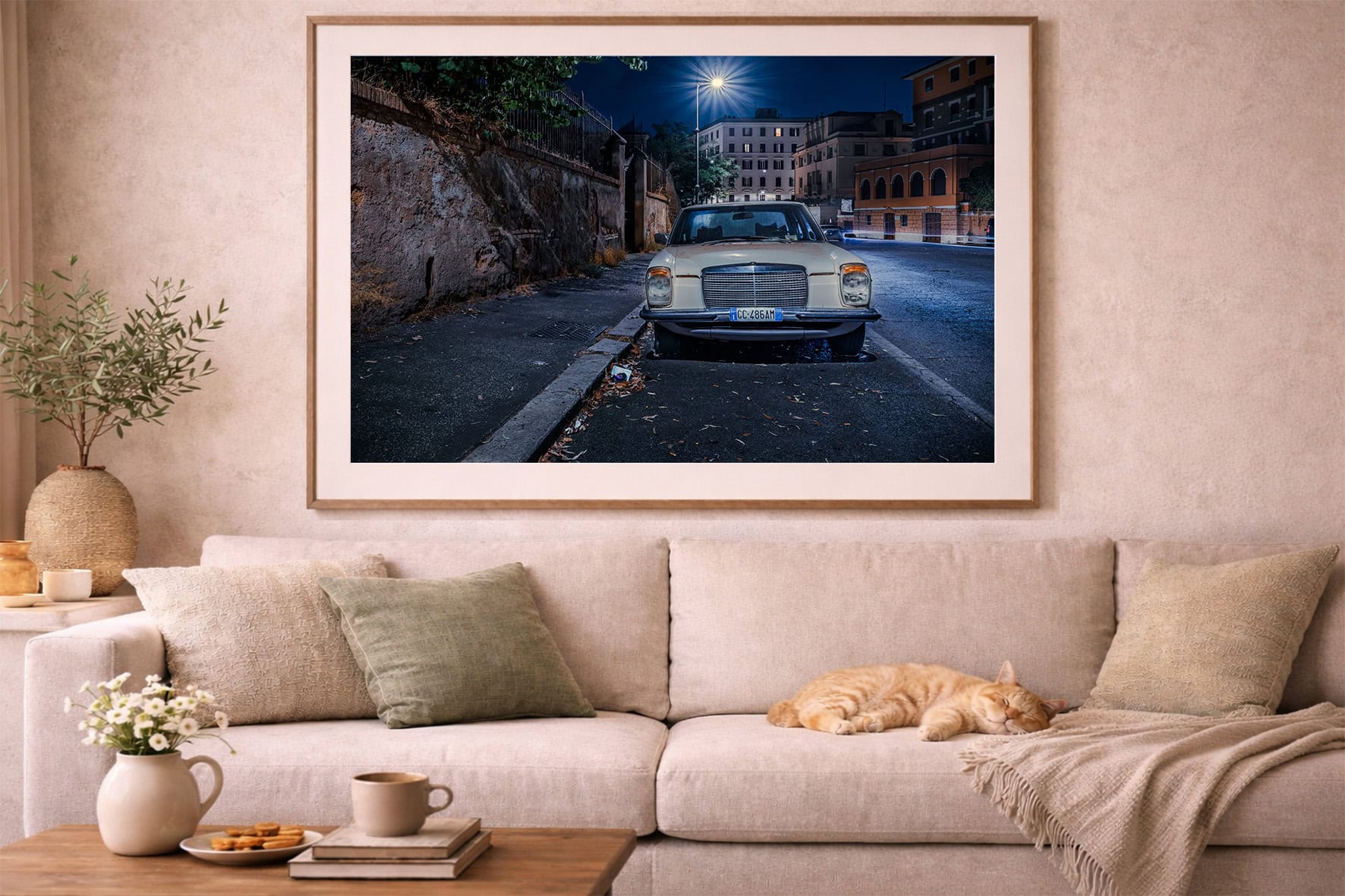 Fotografie eines geparkten Oldtimers in einer nächtlichen Stadtstraße in hellem Rahmen über beiger Couch im Wohnzimmer