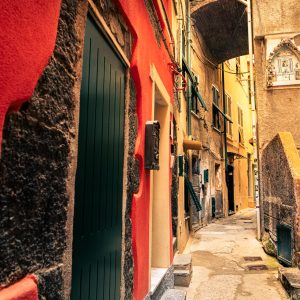 Schmale Gasse in Cinque Terre mit roter Fassade, grünen Türen, Treppe und dicht stehenden Häusern