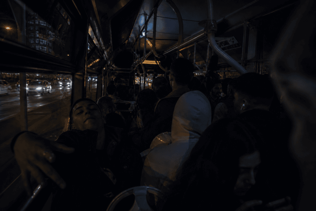Dunkle, volle Buskabine bei Nacht, Menschen stehen eng beisammen, draußen ziehen Autos und Lichter vorbei