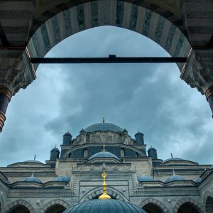 Blick durch einen Arkadenbogen auf eine Moschee in Istanbul mit Kuppeln, Säulen und wolkigem Himmel