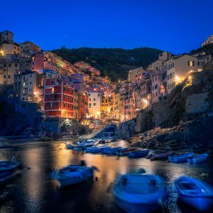 Riomaggiore in Cinque Terre bei Abenddämmerung mit Fischerbooten im Hafen und beleuchteten Häusern