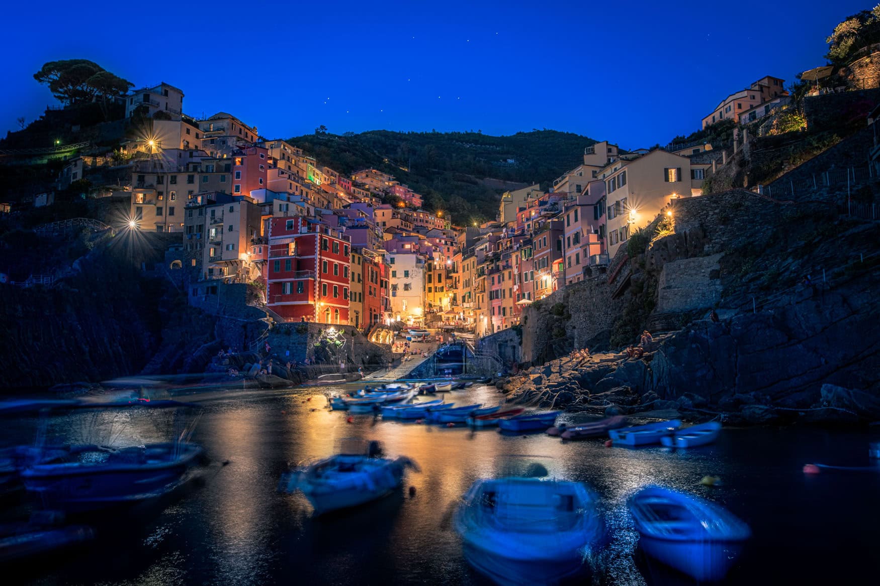 Riomaggiore in Cinque Terre bei Abenddämmerung mit Fischerbooten im Hafen und beleuchteten Häusern