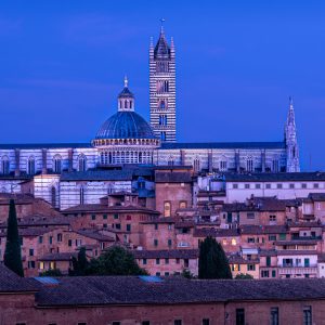 Dom von Siena mit Kuppel und gestreiftem Turm über der Altstadt in blauem Abendlicht