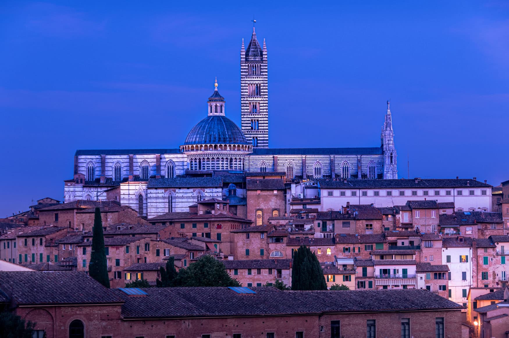 Dom von Siena mit Kuppel und gestreiftem Turm über der Altstadt in blauem Abendlicht