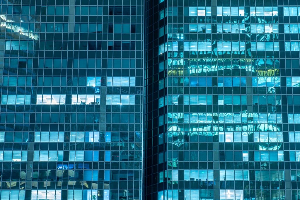 Glasfassaden von Hochhäusern in La Défense Paris bei Nacht mit blauen Spiegelungen und beleuchteten Fenstern