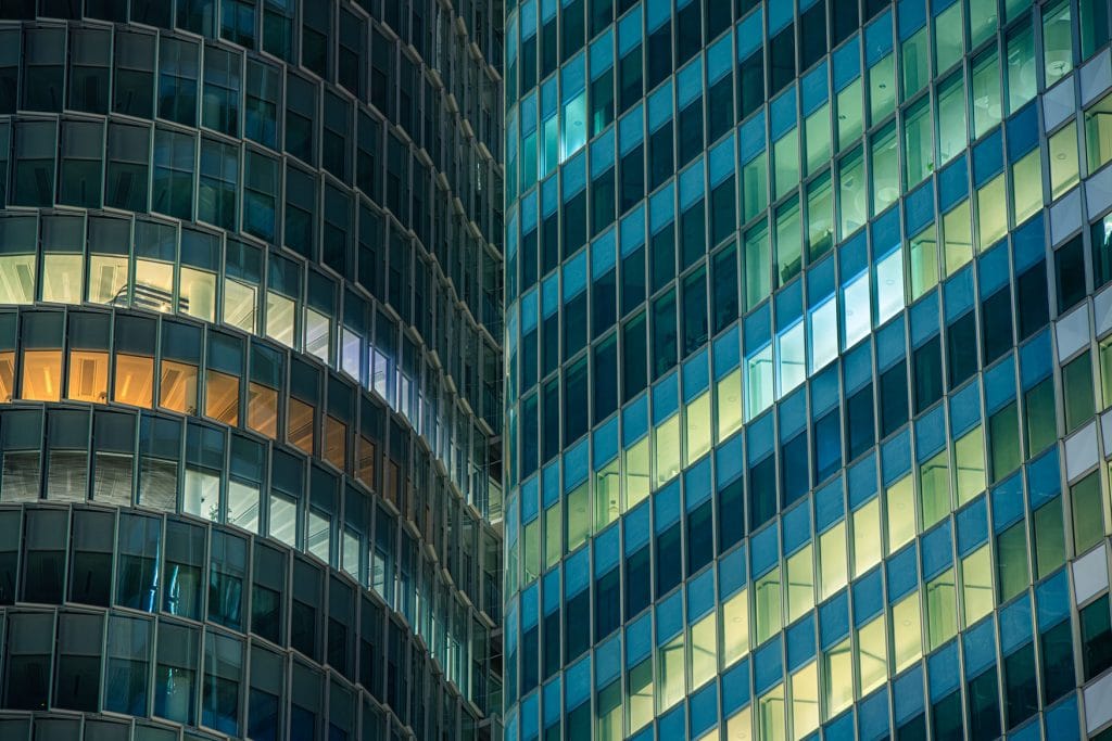 Gläserne Hochhausfassaden in La Défense Paris bei Nacht mit beleuchteten Fenstern in Blau- und Grüntönen