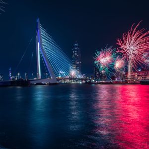 Feuerwerk über der Erasmusbrücke in Rotterdam bei Nacht mit farbigen Spiegelungen auf dem Wasser