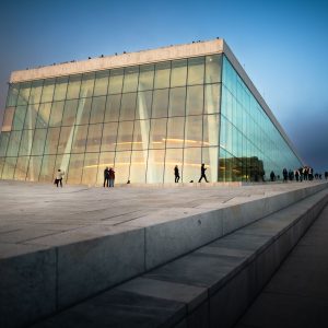 Gläserne Architektur des Osloer Opernhauses in der Abenddämmerung mit Menschen auf der hellen Steinfläche