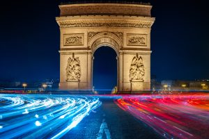 Arc de Triomphe in Paris bei Nacht mit roten und blauen Lichtspuren im Kreisverkehr