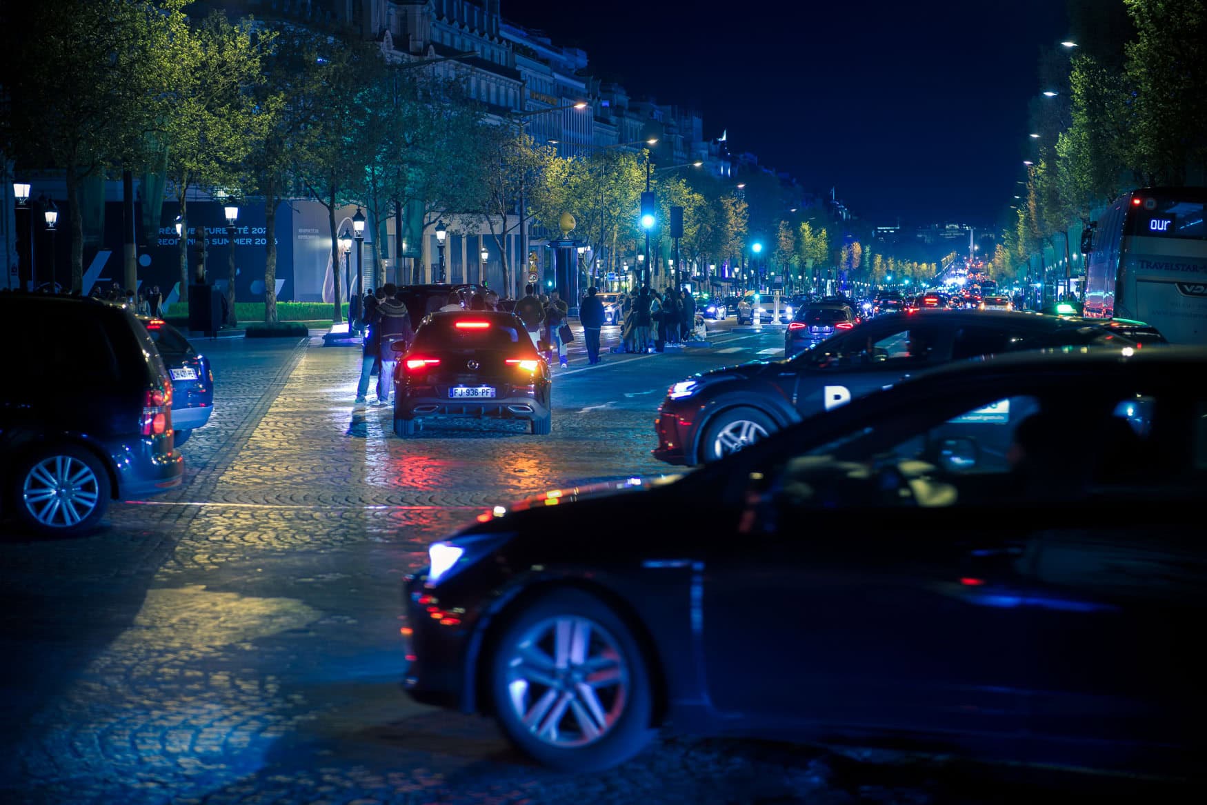 Nachtverkehr in Paris auf breiter Allee mit Autos, Bäumen, Straßenlaternen und leuchtender Fahrbahn