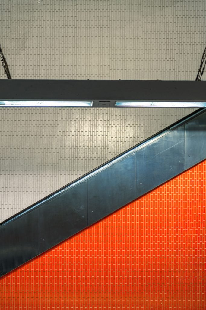 Schräg verlaufende Rolltreppe in der Metrostation Gabriel Péri in Paris vor orange-weißer Fliesenwand