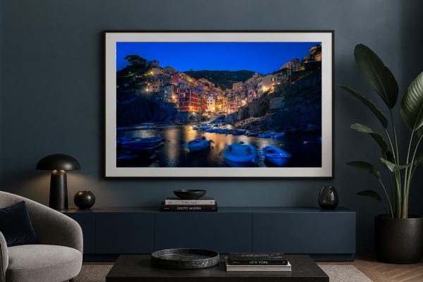 Fotografie einer beleuchteten Küstenstadt bei Nacht mit Booten im Hafen, gerahmt über einem dunklen Sideboard in modernem Wohnzimmer
