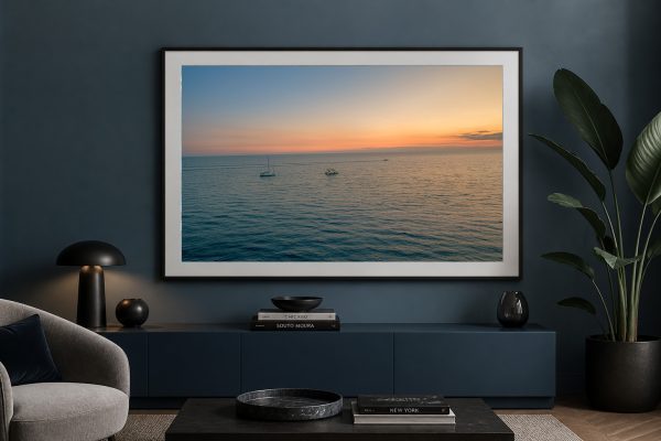 Großer gerahmter Fotodruck mit ruhigem Meer und zwei Booten bei Sonnenuntergang in einem dunklen, modernen Wohnzimmer.