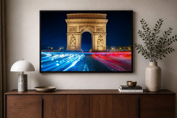 Fotografie eines beleuchteten Triumphbogens bei Nacht mit blauen und roten Lichtspuren, gerahmt über einem Holzsideboard im modernen Wohnzimmer.