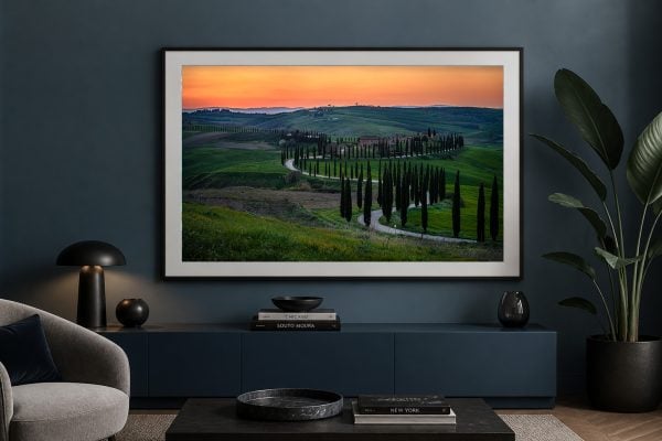 Großformatige Fotografie einer kurvigen Zypressenallee in grünen Hügeln bei Sonnenuntergang, gerahmt über einem dunklen Sideboard im modernen Wohnzimmer