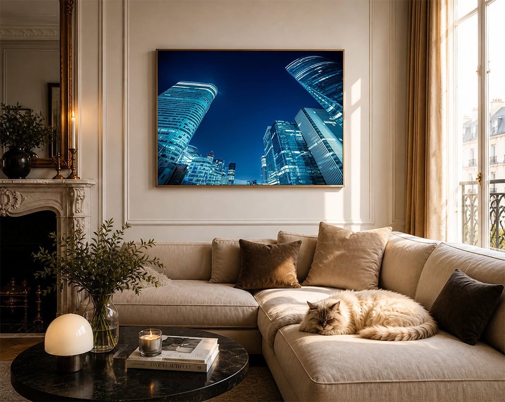 Fotografie moderner Glaswolkenkratzer bei Nacht in Blau, gerahmt über einem eleganten Wohnzimmer-Sofa mit schlafender Katze.