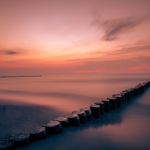 Ruhige Ostsee bei Zingst mit hölzernen Buhnen, glattem Wasser und rosafarbenem Himmel