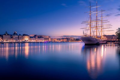 Fine-Art-Print Stockholm Skyline mit beleuchtetem Segelschiff bei Sonnenuntergang, erhältlich als hochwertiger Kunstdruck.