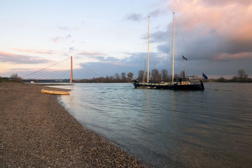 Segelschiff vor der Fleherbrücke bei Düsseldorf am Rheinufer bei Abendlicht
