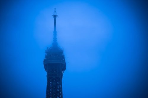 Spitze des Eiffelturms in Paris, von blauem Nebel umhüllt zur Blauen Stunde